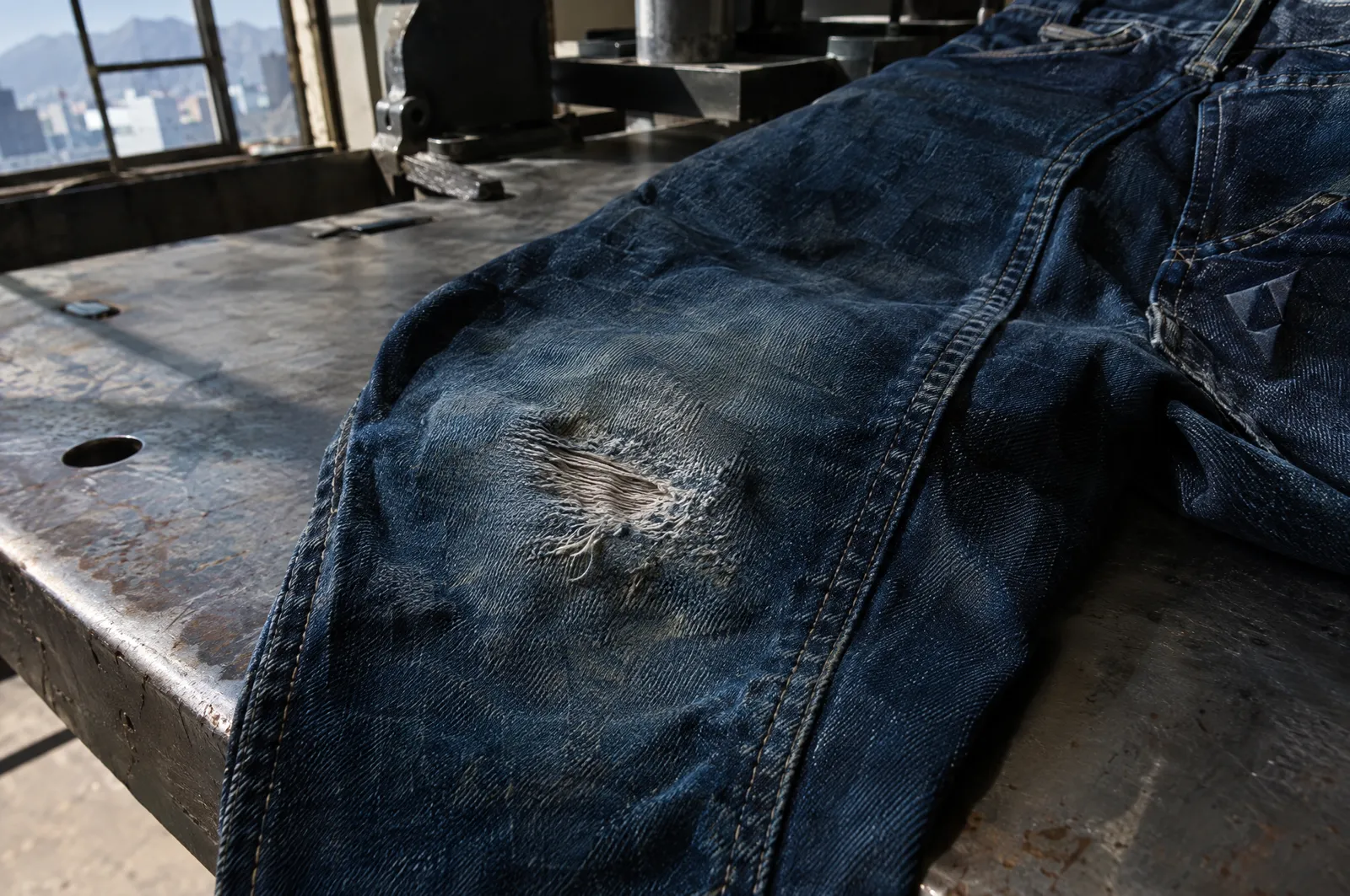Rodilla gastada y adelgazada de un pantalón de mezclilla de trabajo sobre una mesa de taller